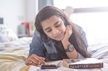 Female student reading and usif mobile phone on bed
