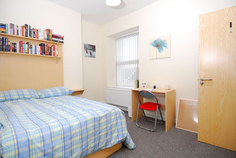 Premium en-suite room having bed, books in the wall shelf and study table