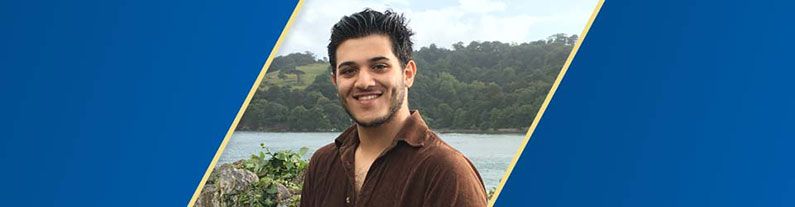 A male student smiling and standing outside